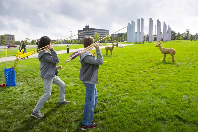 Two kids throwing spears at practice deer outside.