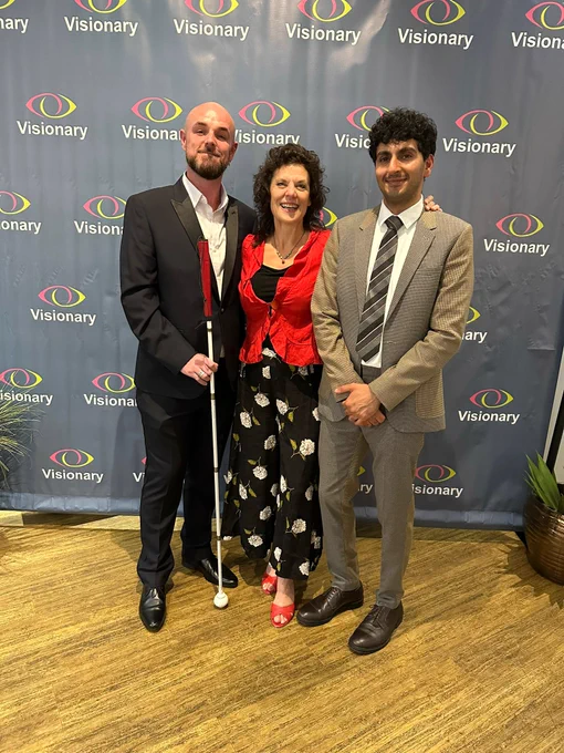 Justin, Sharon and Amrat standing together smiling in front of a Visionary Background