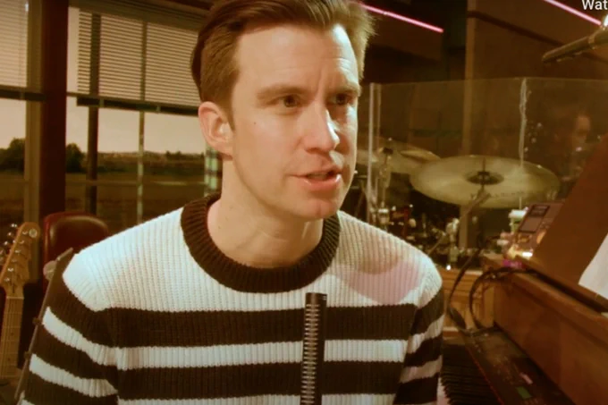 A photo showing a man speaking in front of a band equipment stall 