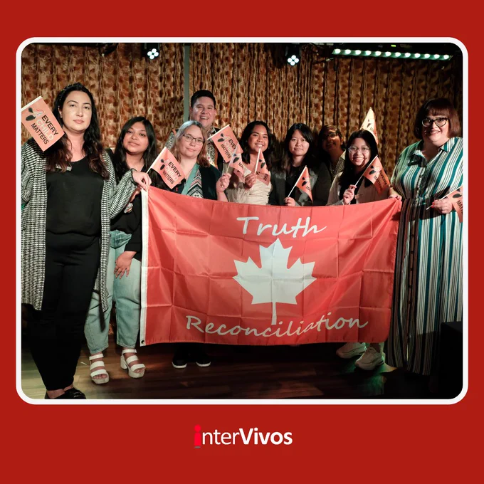 interVivos Board members, volunteers, and MLA Brooks Arcand-Paul hold orange flags at 99ten to show they are committed to reconciliation and healing. The image has  a red frame with a white border. 