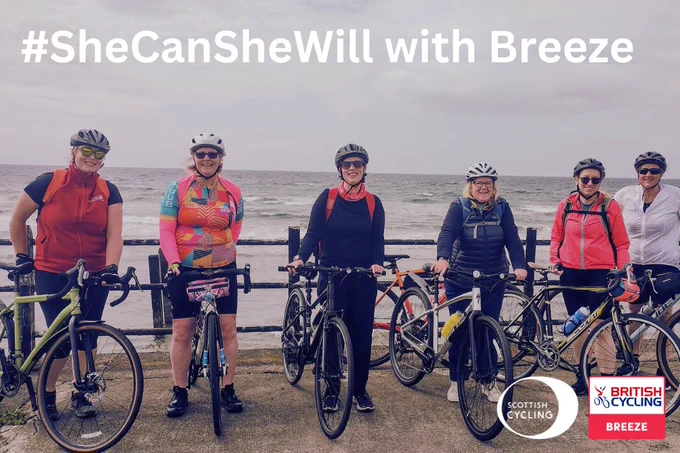 A group of six women cyclists standing with their bikes in front of a coastal background, smiling and dressed in cycling gear. The text reads '#SheCanSheWill with Breeze.' Logos for Scottish Cycling and British Cycling Breeze are displayed in the bottom-right corner.