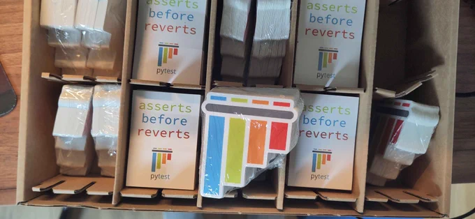 A box full of pytest panflute logo stickers and "sserts before reverts" stickers.