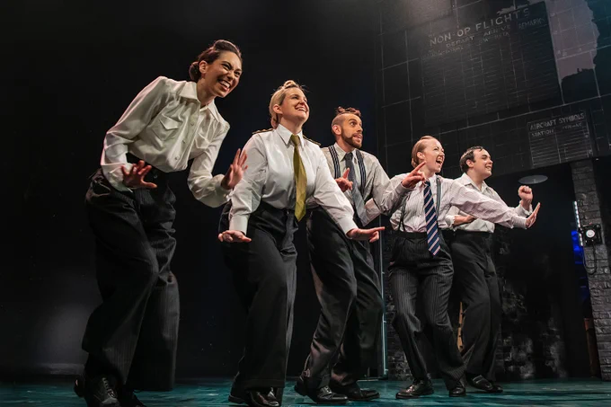A photo showing five performers in shirts and ties dancing on a stage