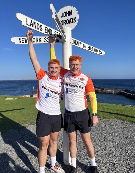 Jordan & Cian in front of the iconic John O'Groats signpost, indicating distances to Land's End.