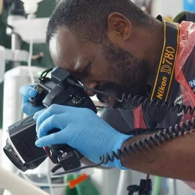 A close up shot of Karel who is taking a photograph using a camera. He is wearing blue rubber gloves.