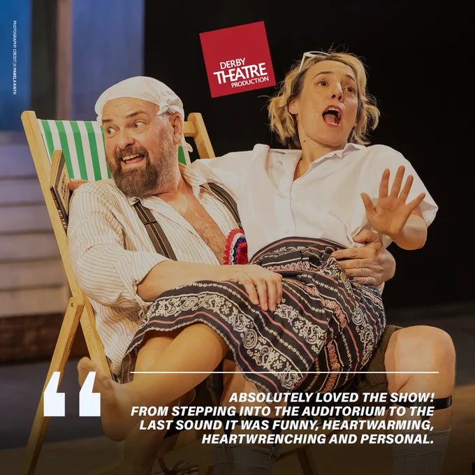 A lighthearted moment from a stage production. A bearded man, wearing suspenders and a bandana on his head, relaxes in a deck chair. A woman, sitting beside him on his lap, appears surprised and animated. Both actors are dressed casually, with the woman wearing a white shirt and patterned skirt. The mood is cheerful and humorous. The Derby Theatre logo is visible at the top, and the quote below reads, "Absolutely loved the show! From stepping into the auditorium to the last sound it was funny, heart-warming, heart wrenching and personal."