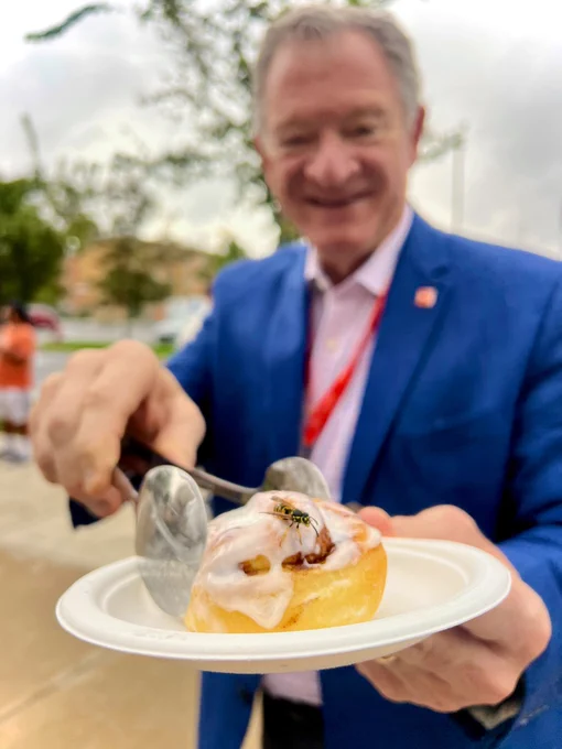 BGSU President Rogers holding a cinnamon roll with a yellow jacket on it