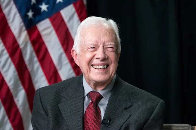 Photo of President Jimmy Carter. He is sitting in front of an American flag.