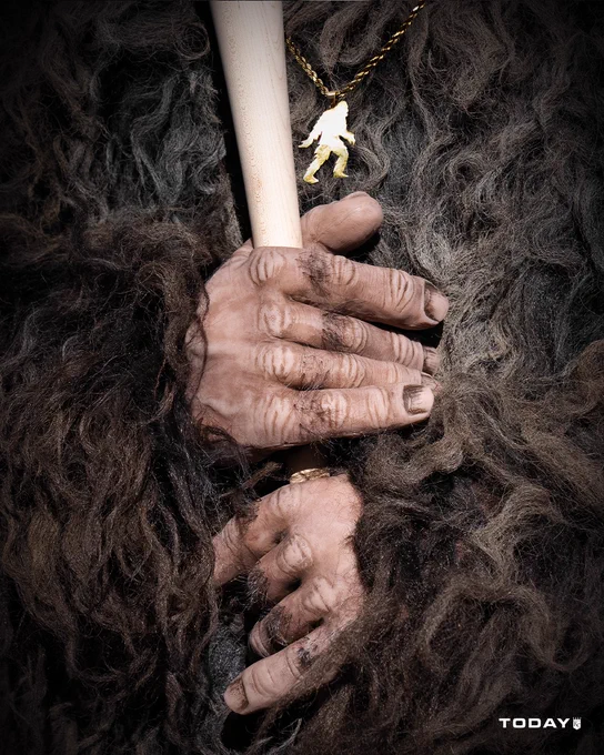 A close-up photo of the Pasquatch holding a baseball bat. A Pasquatch chain hangs around its neck.