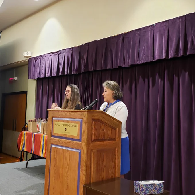 Rosalyn Tso, Director of Indian health services, standing at a Brownwood podium in a blue dress with a white cardigan. Speaking into the microphone.