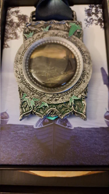 The backside of the medal shows a hazy picture of a burned village. Elvish writings circle around that picture. Green leaves are engraved at the top and bottom of this side of the medal.