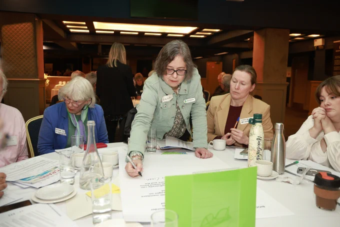 Photograph of four delegates at a round table - one delegate is standing and writing notes.