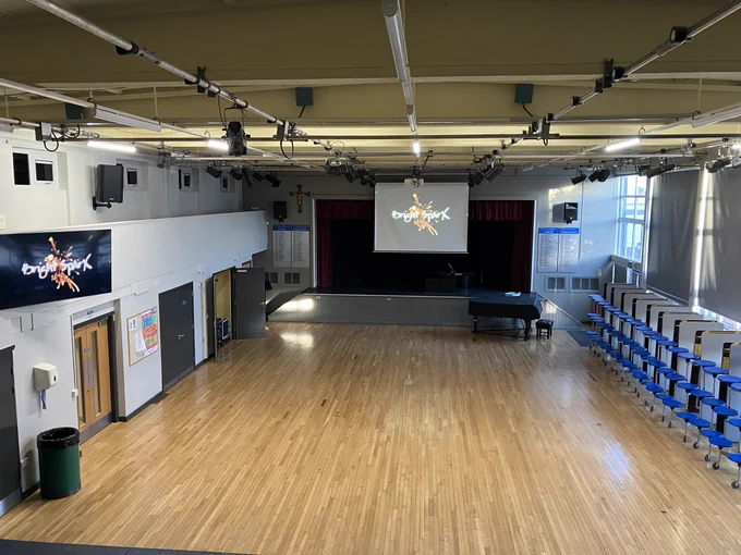 Picture of school hall, with Bright Sparx presentation slide open, which is displayed on a large screen and large TV.