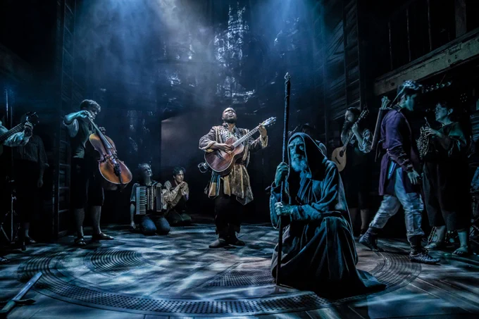 A photo showing a group of performers on a dimly-lit stage in fantastical robed outfits on a stage 