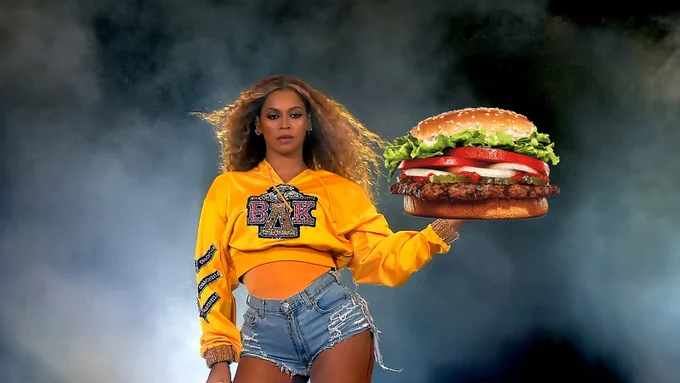 Beyonce Knowles in a yellow top and hotpants holds a giant burger