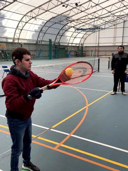 A player with a visual impairment serving a tennis ball at our session.