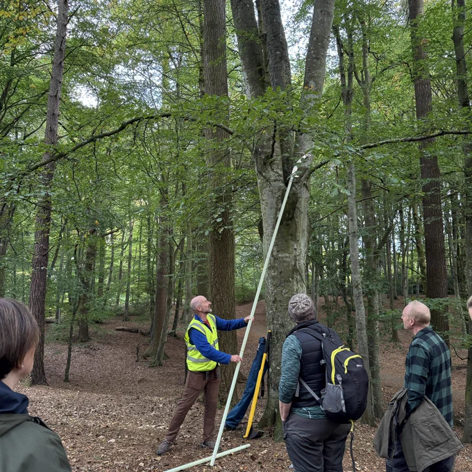 A member of Culduthel Community Woods demonstrates the use of a pole saw tool to a small group of people in their woodland.