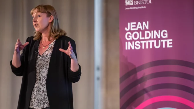 Professor Genevieve Liveley in front of a Jean Golding Institute banner