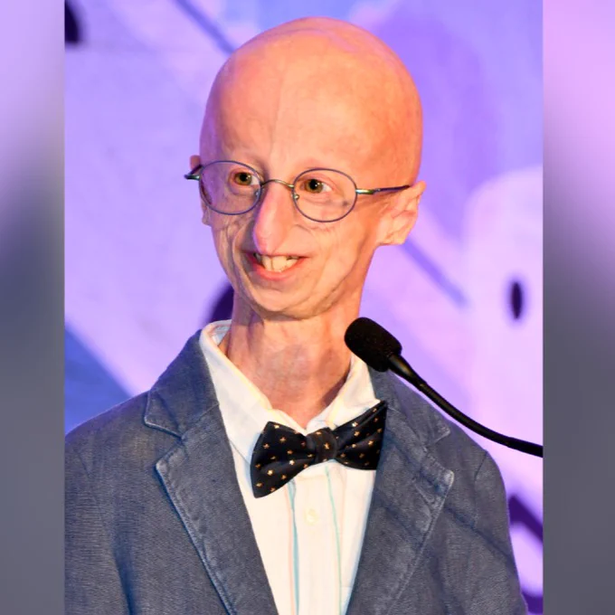 Sammy Basso speaking at a podium at a Progeria Research Foundation event.