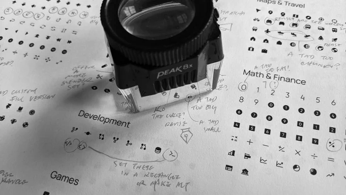 A printed sheet of paper with dozens of icons with notes and markup, with a loupe