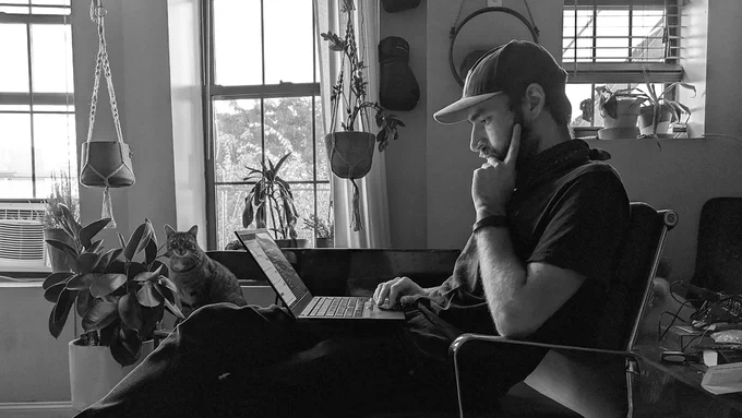 Toby thinking deeply while staring at his laptop screen, cat in the background