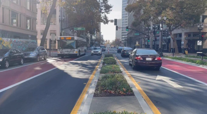 A view down Oakland’s Broadway, looking south near the intersection of Telegraph. The roadway has a small grassy median, with two general traffic lanes, a bus lane, and a parking lane. An AC Transit 72R bus is driving north on Broadway.

Image credit: City of Oakland “Broadway Bus Lanes & Pedestrian Safety Improvements”