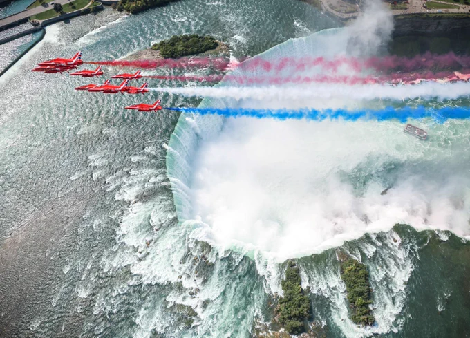 RAF Red Arrows flying over Niagara Falls, with their iconic blue, white, and red smoke trailing behind.