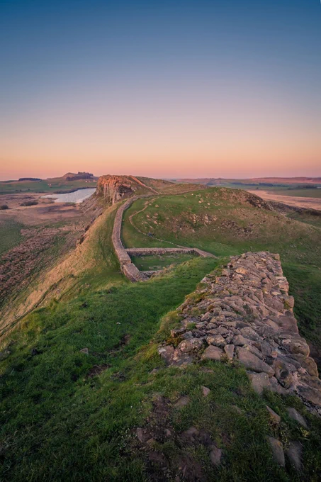 a stone wall on a grassy hill with a river in the distance
