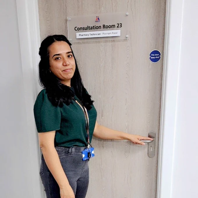 A photograph of Poonam standing outside her pharmacy consultation room. Her name is written on the door. 