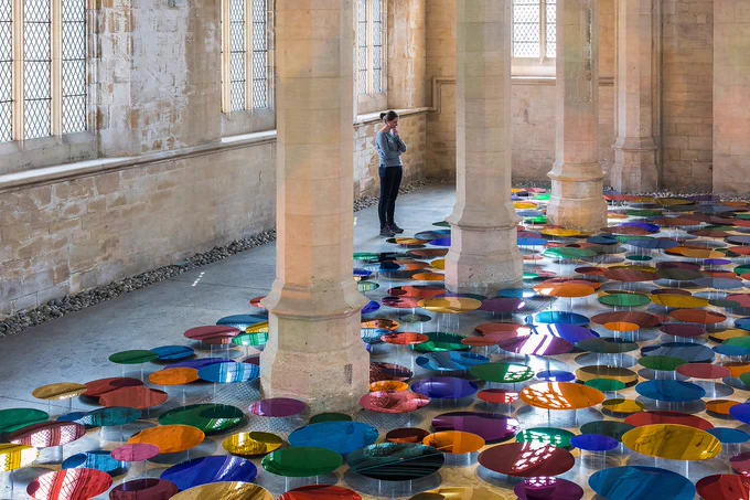 An installation of rainbow coloured mirrored discs displayed on the floor of a chapel.