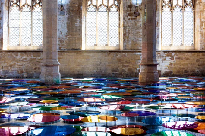 An installation of rainbow coloured mirrored discs displayed on the floor of a chapel.