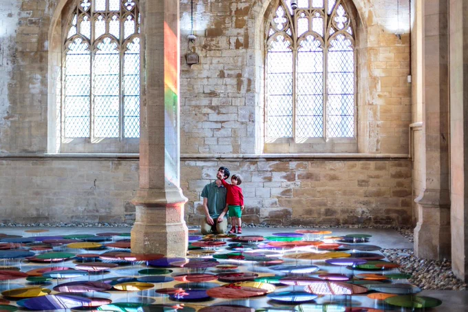 An installation of rainbow coloured mirrored discs displayed on the floor of a chapel.