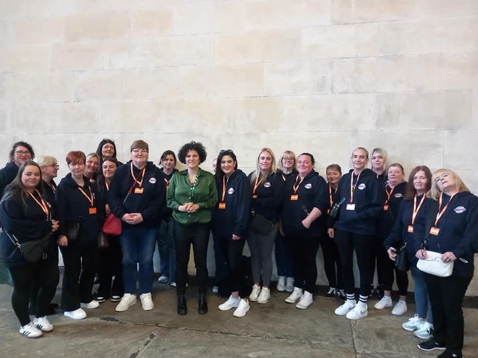 Group of women in navy ‘changemaker’ hoodies with Claire Hanna MP in Westminster Hall.