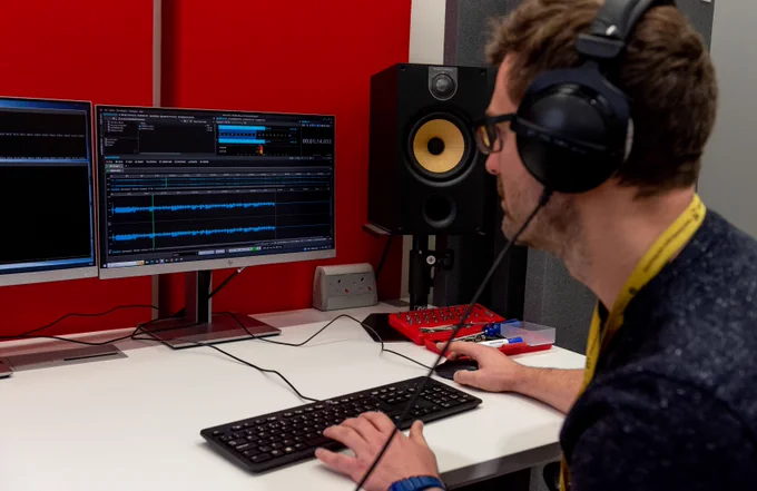 A person wearing head phones editing sound waves on a computer monitor.