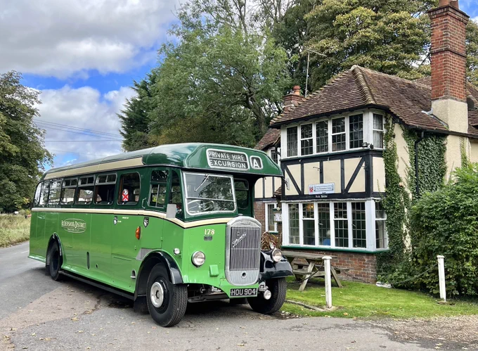 A vintage green bus outside a Tudor style building.