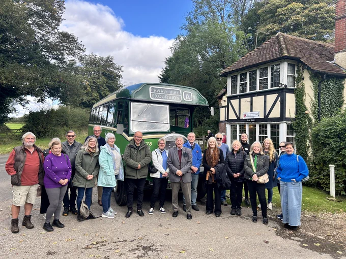 A group of people standing in front of a vintage green bus and Tudor style building.