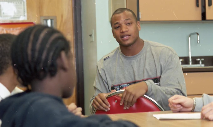 Wes Moore sits backward in a chair and speaks to two teens. 