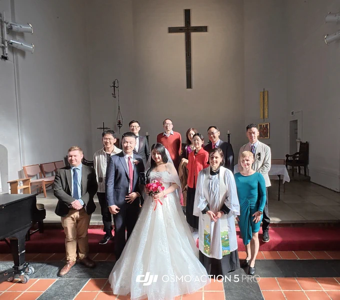 A gathering of people at a wedding ceremony inside a chapel, with a cross in the background