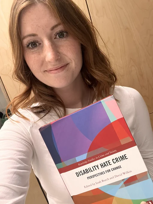 Selfie of Leah with the book titled Disability Hate Crime: Perspectives for Change