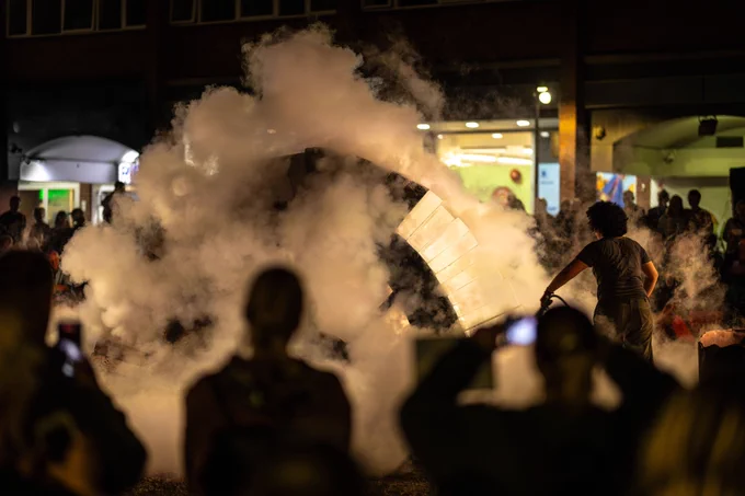 All of the blocks of the arch are in place. Nao sprays the structure with carbon dioxide from a fire extinguisher, preparing to remove the supporting former underneath it. Audiences crane their necks to look and film with their phones as the gas rises around the arch.