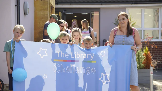 Children holding up a banner outside a library saying 'The Library Challenge'