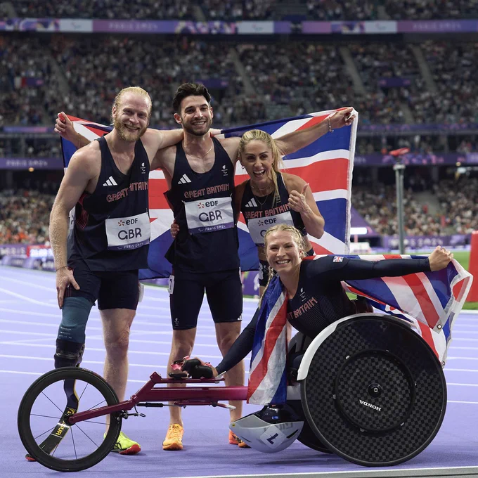 Four ParalympicsGB athletes from the universal relay team with a leg amputation, visual impairment, cerebral palsy and a wheelchair racer with the Union flag in the athletes stadium in Paris after a race