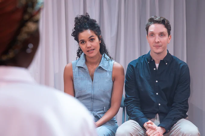 Alice (Emma McDonald) and Jay (Christopher York) sit in front of a clinical grey background talking to a doctor (Valerie Antwi)