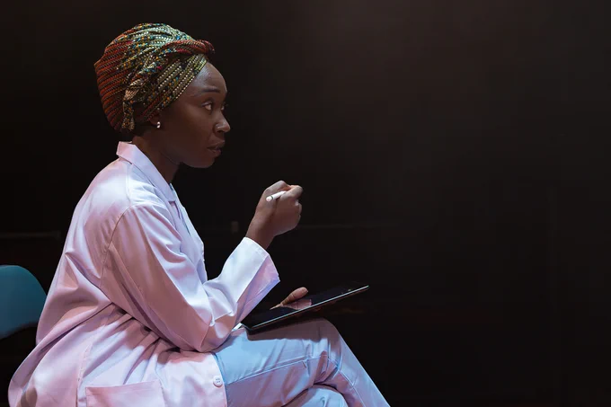 A Doctor sits holding a tablet, looking directly ahead in an intense manner