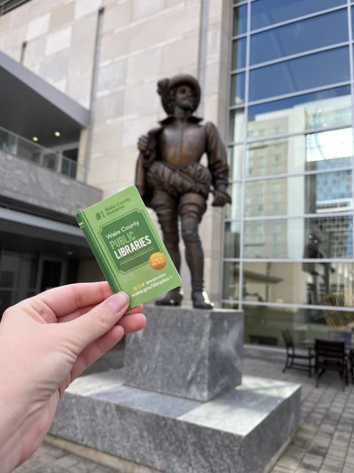 A hand holding up a library card near a statue