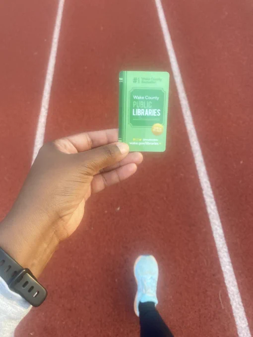 A hand holding up a library card on a running track
