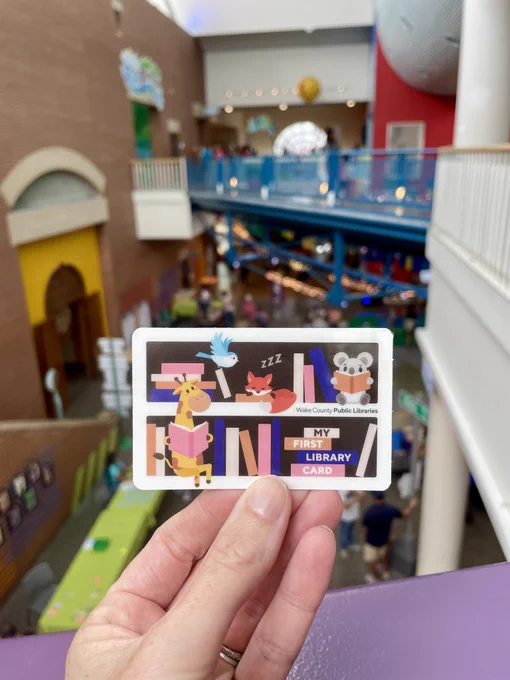 A hand holding up a library card in Marbles Kids Museum
