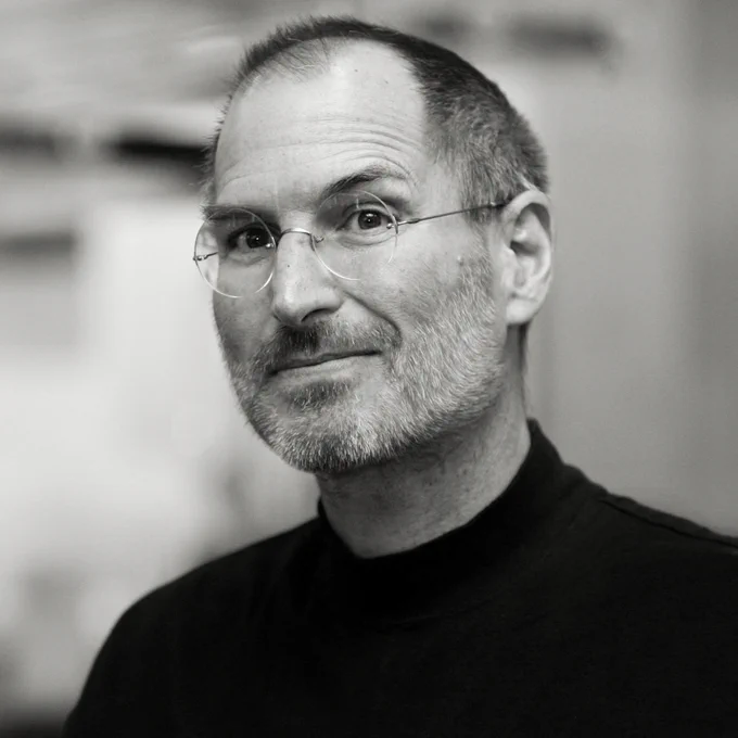 A black and white portrait of Steve smiling in glasses and a black turtleneck from 2007. 
