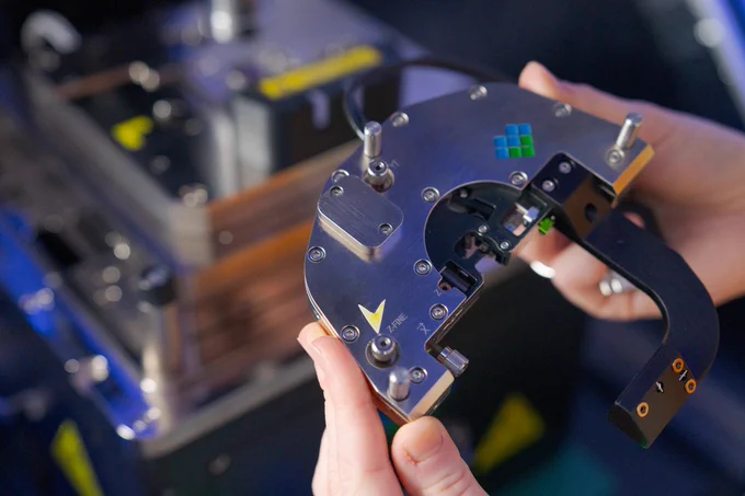  Dr. Otter hold a critical piece of a microscope with neon visual markers on it in bright blue and green colours. The background is a blurred piece of equipment from the Photo-induced Force Microscopy lab. Photo: Nic Vevers/ANU