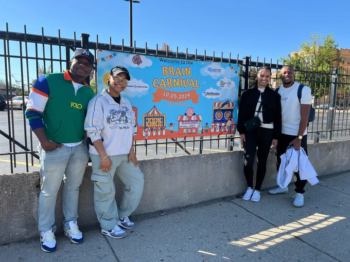 A picture of Timi, Paige, Clíona and De-Shaine posed outside the gates of a church next to the Brain Carnival poster. 